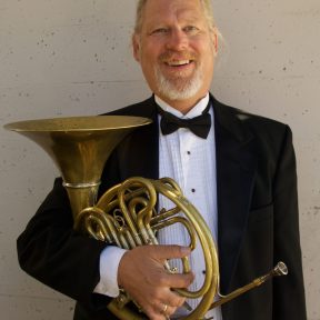 Horn player Jeff Fowler poses holding his horn while wearing a tux.