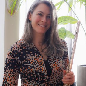 Vitoria Hauk poses with her flute in front of potted plants and a sunny window.