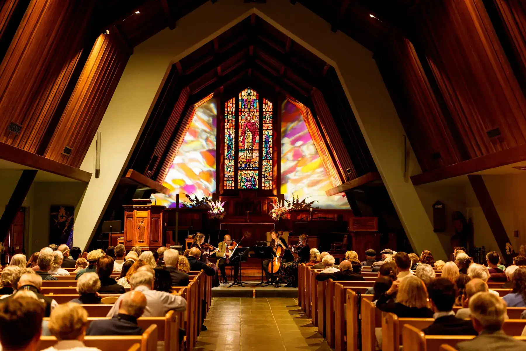 A string quartet performs before the stained-glass altar window at All Saints’ Episcopal Church as an audience listens from the pews.