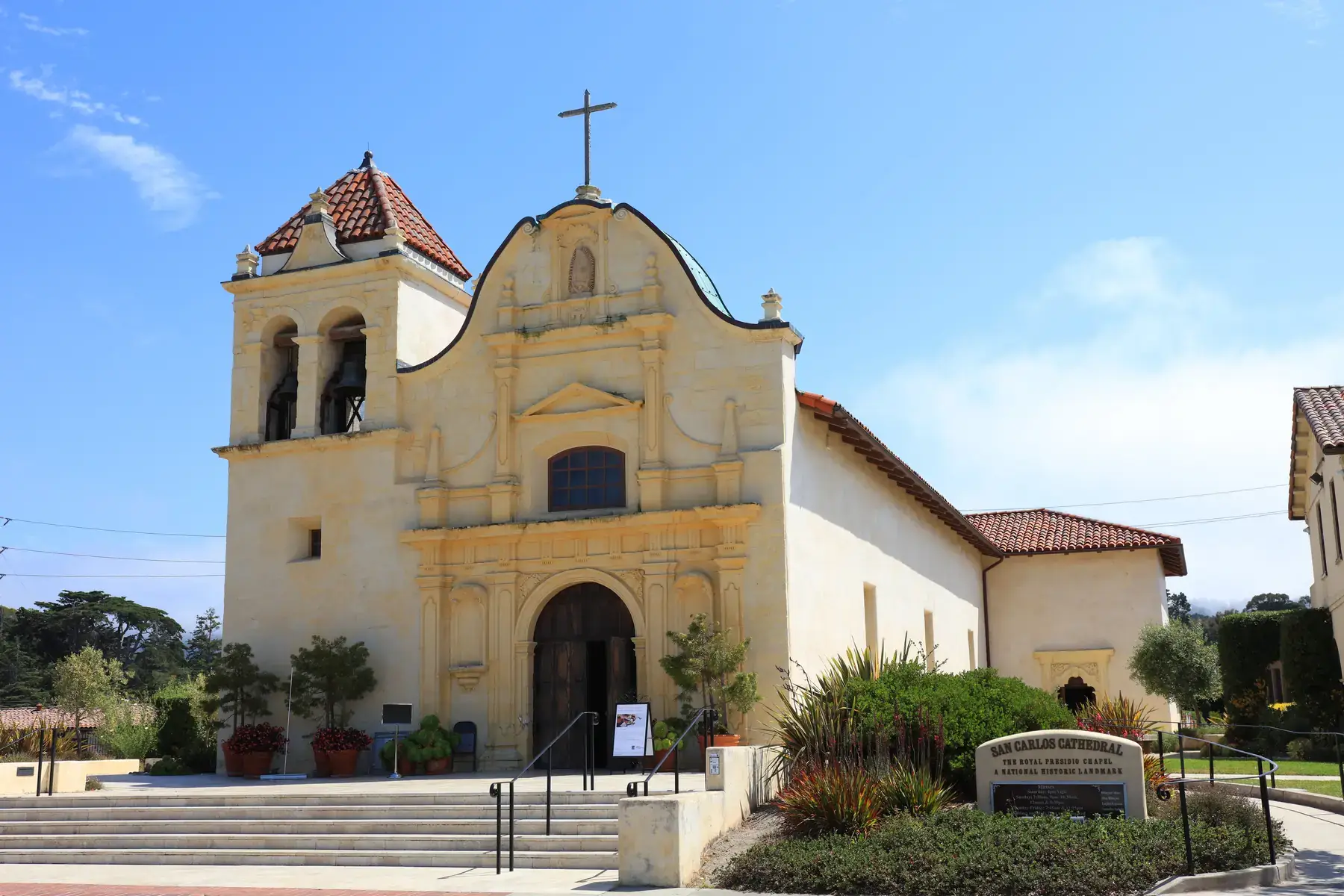The cream-colored baroque facade and bell tower of San Carlos Cathedral, the Royal Presidio Chapel, under a blue sky.