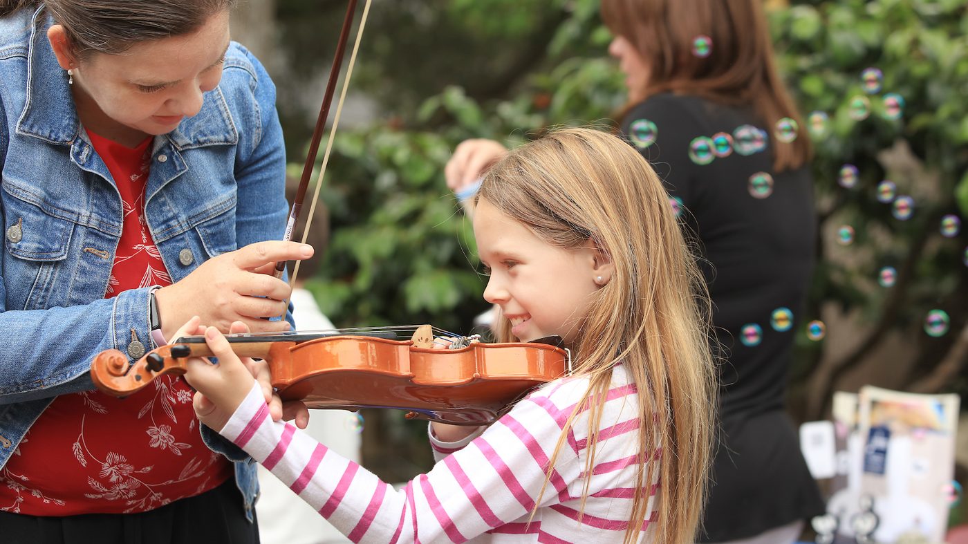 A young student learns to hold a violin with help from a teaching artist