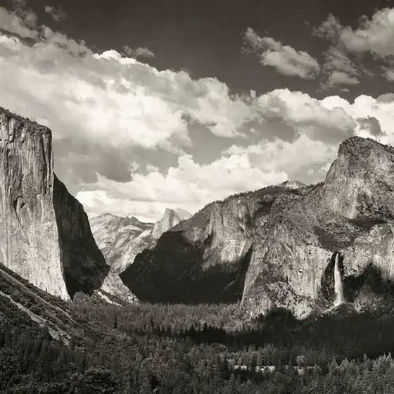 Black-and-white photograph of a granite valley with a waterfall, under towering clouds